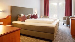 A hotel room with a large bed, a desk, a chair, and a window with curtains. - Hotel Victoria (Bad Kreuznach)