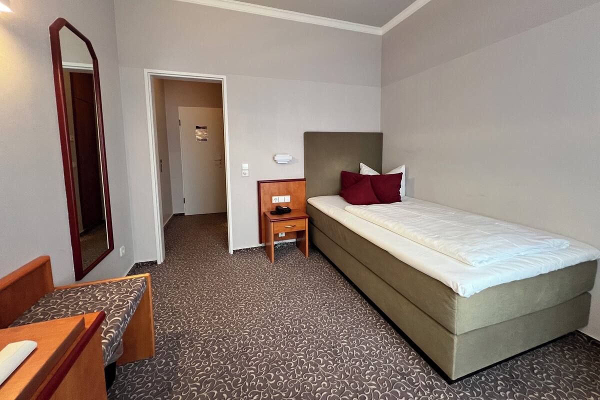 A hotel room with a bed, bedside table, and a mirror.