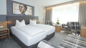 A modern hotel room with a large bed, a desk, a chair, and a sofa.