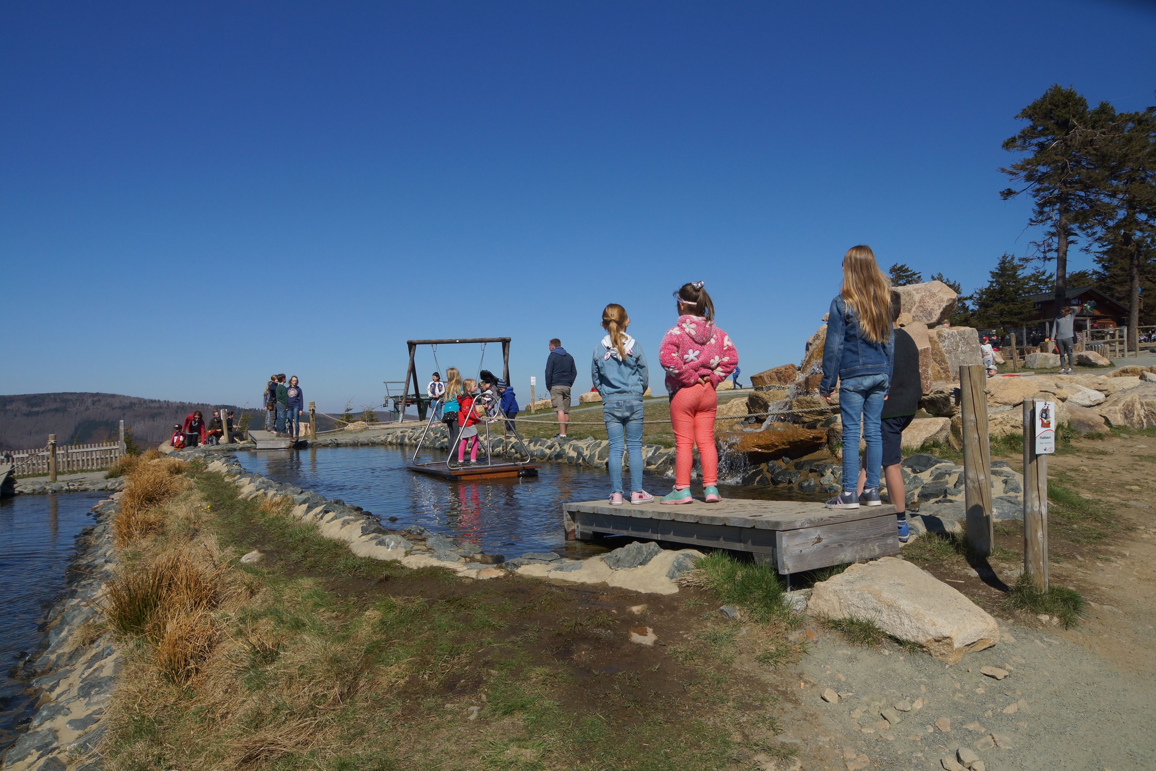 A group of people near a water body with a wooden platform and a swing set.
