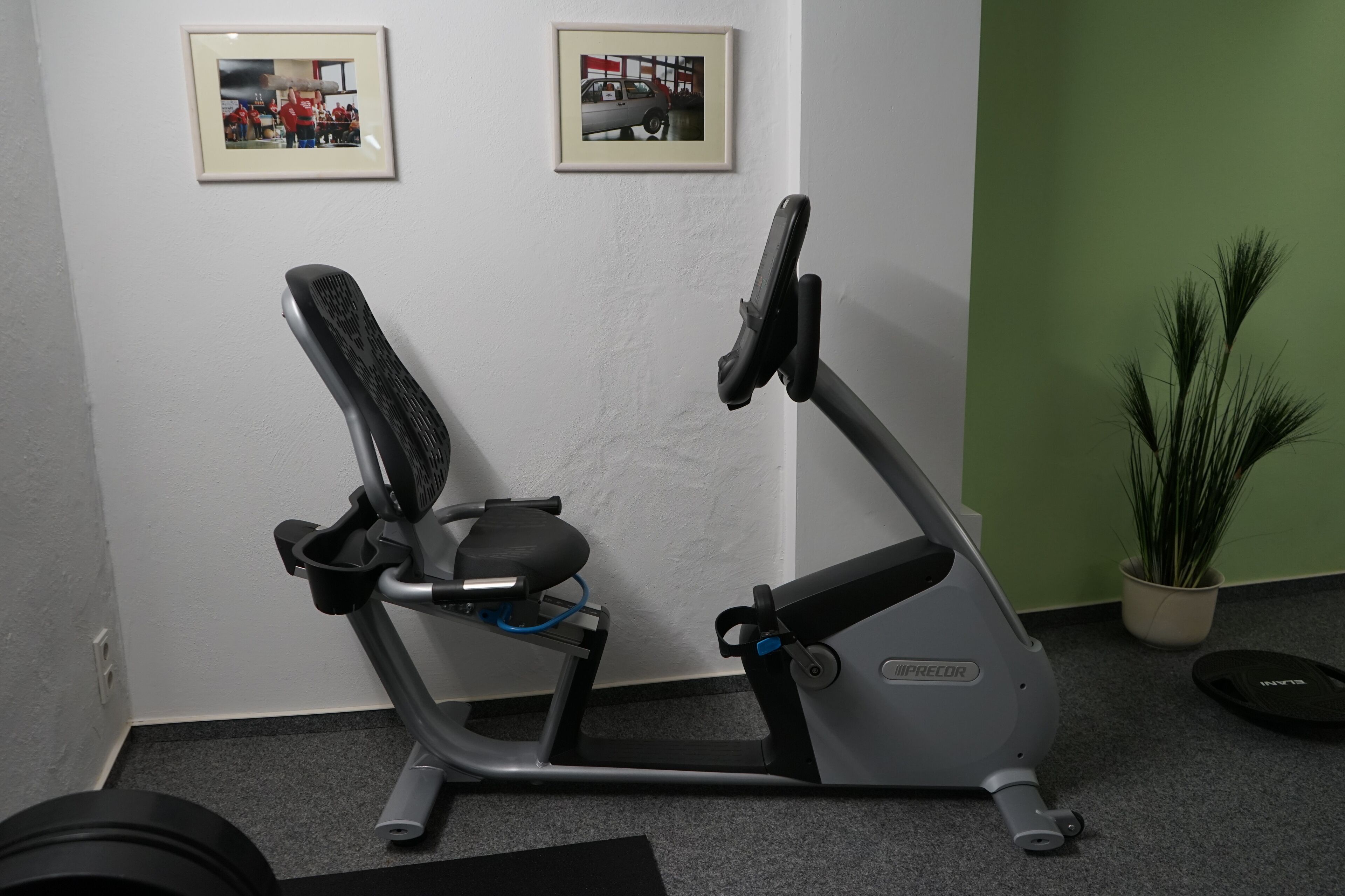 An exercise bike in a room with a green wall and two framed pictures.