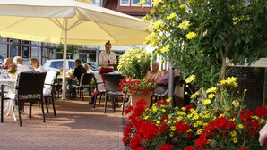 An outdoor seating area with tables and chairs under umbrellas, surrounded by potted plants with red and yellow flowers.