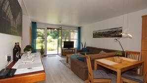 A modern living room with a wooden dining table, a sofa, and a TV on a stand. - Komforthotel & Restaurant Riemann (Bad Lauterberg)