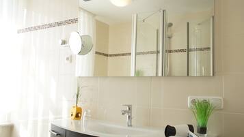 A bathroom with a white sink, a mirror, a glass shower enclosure, and a potted plant.