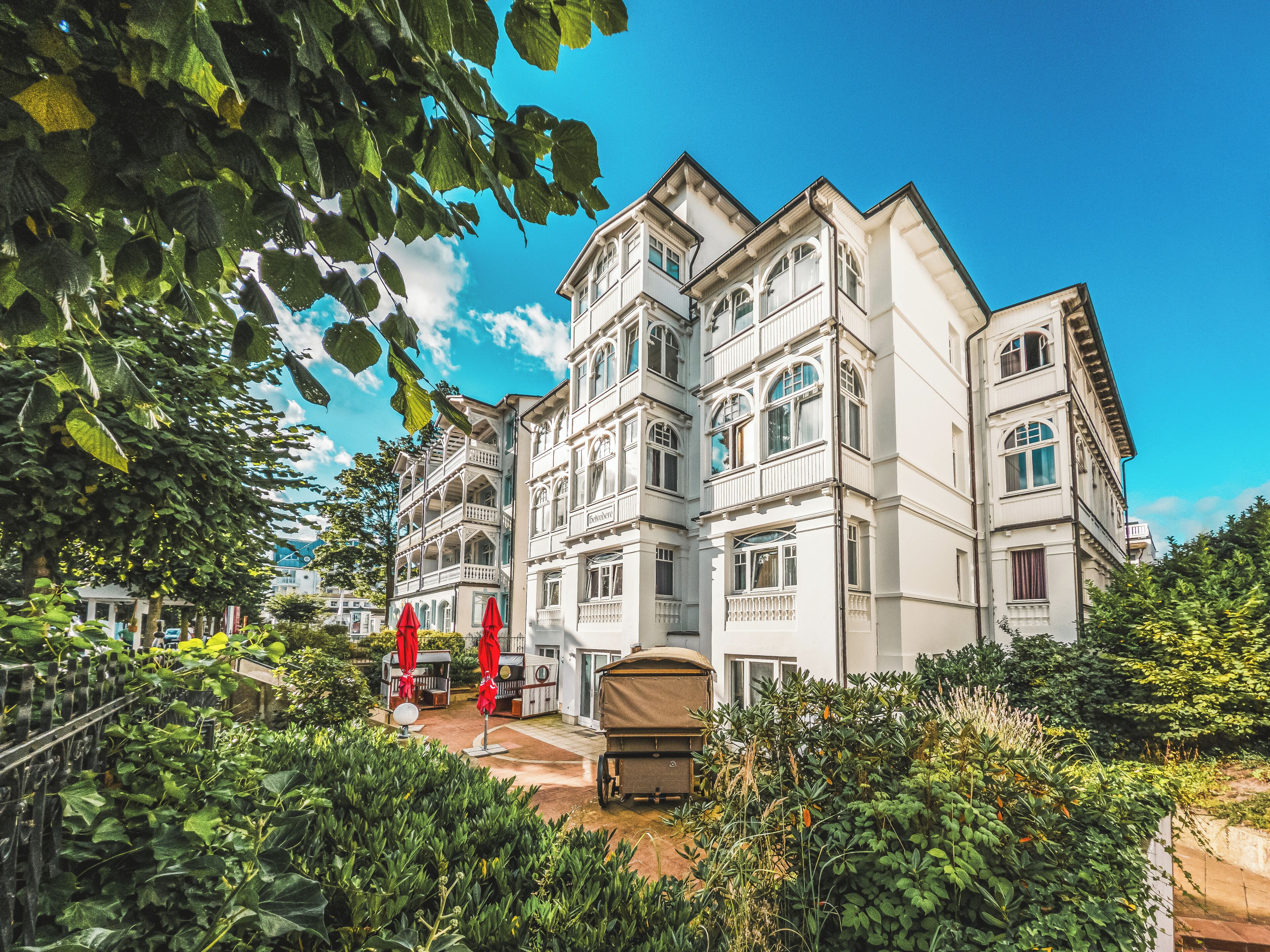 A multi-story building with balconies, a covered outdoor seating area, and lush greenery.
