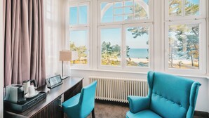 Une chambre d’hôtel équipée d’un bureau, de deux chaises, d’une machine à café et offrant une vue sur la mer grâce à de grandes fenêtres.