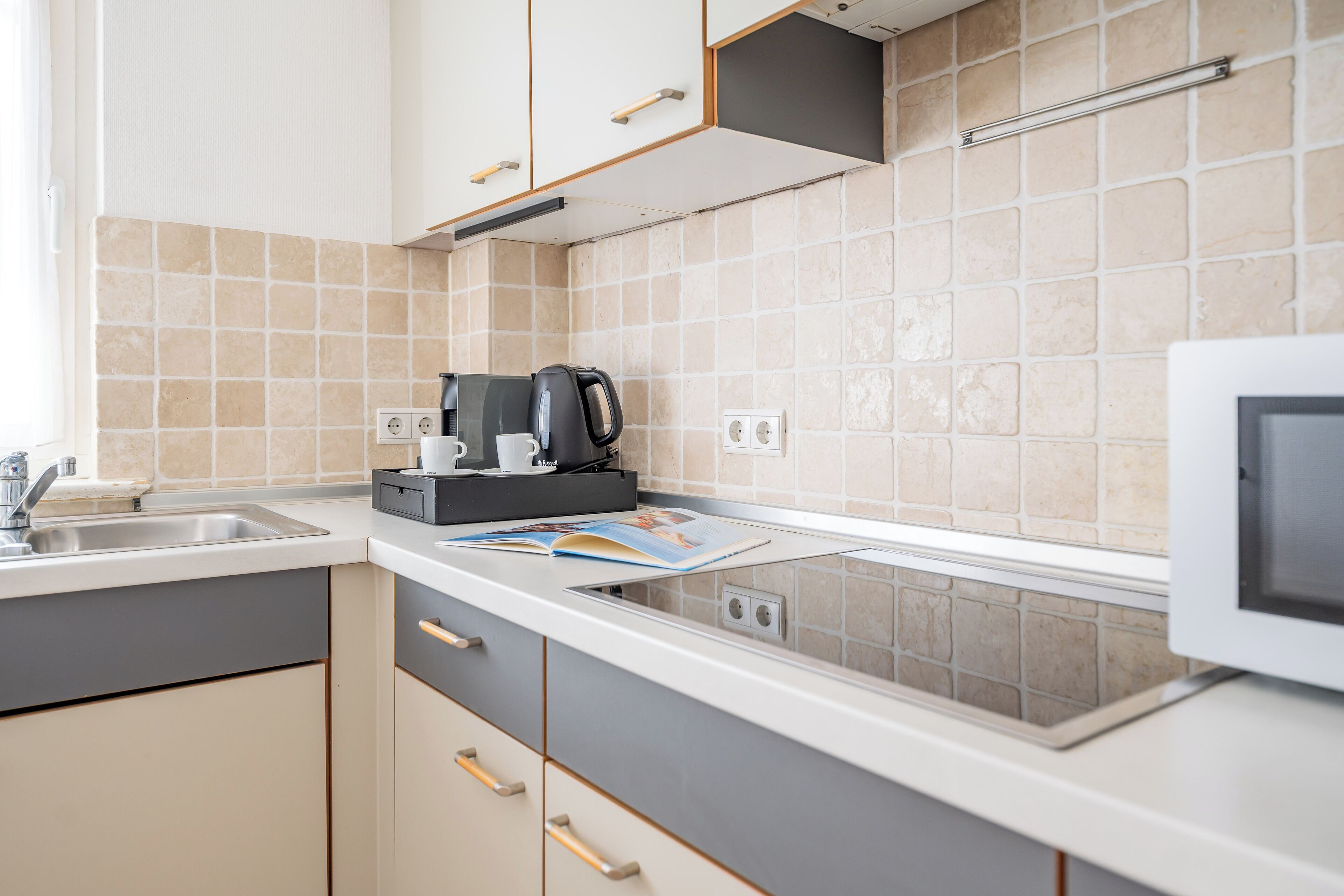 A modern kitchen with a built-in microwave, a coffee maker, and a magazine on the counter.