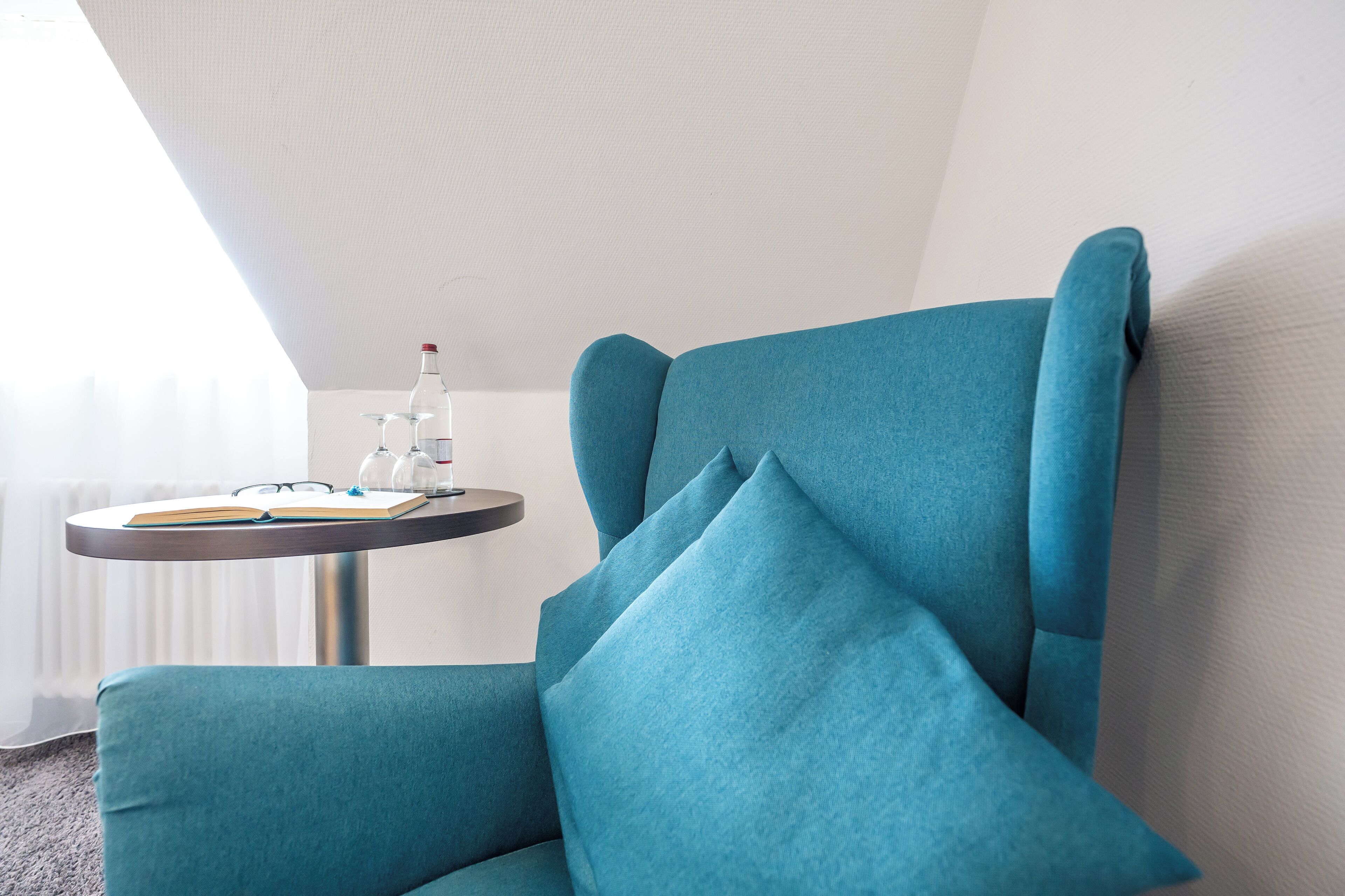 A teal armchair with a small table beside it, a book, and a bottle of water.