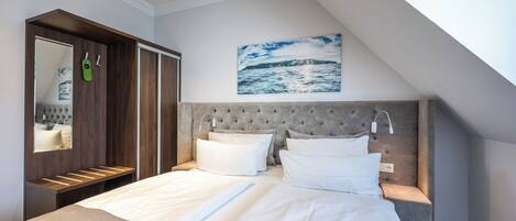 A modern hotel room with a large bed, a built-in wardrobe, a painting of a seascape, and a skylight.