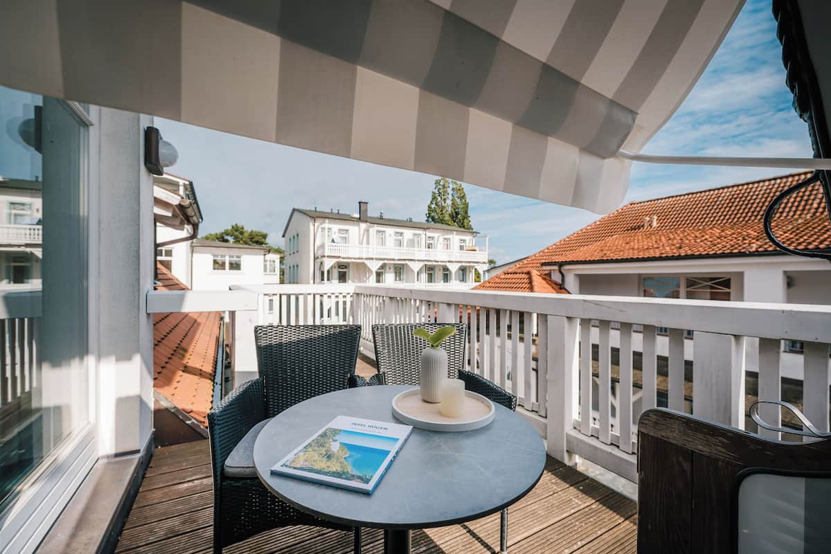 A balcony with a round table, chairs, a book, and a vase.