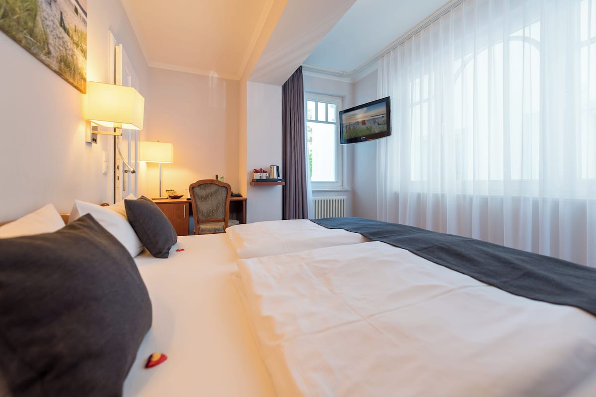 A hotel room with two beds, a desk with a lamp, a chair, a television, and a window with curtains.