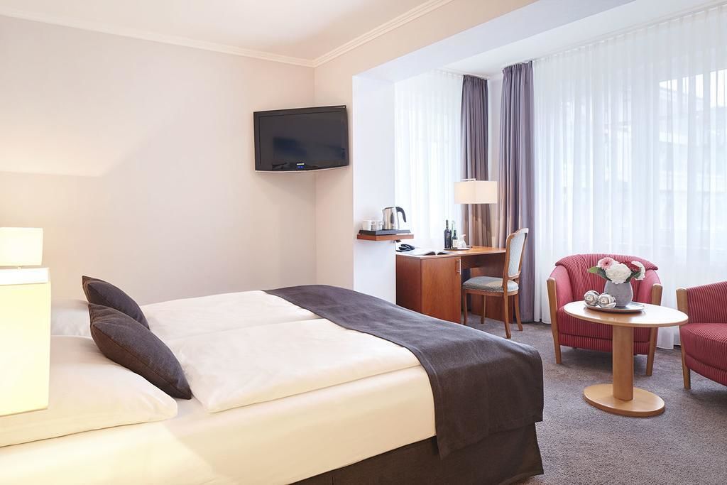 A hotel room with a bed, a desk, a chair, a television, and a window with curtains.
