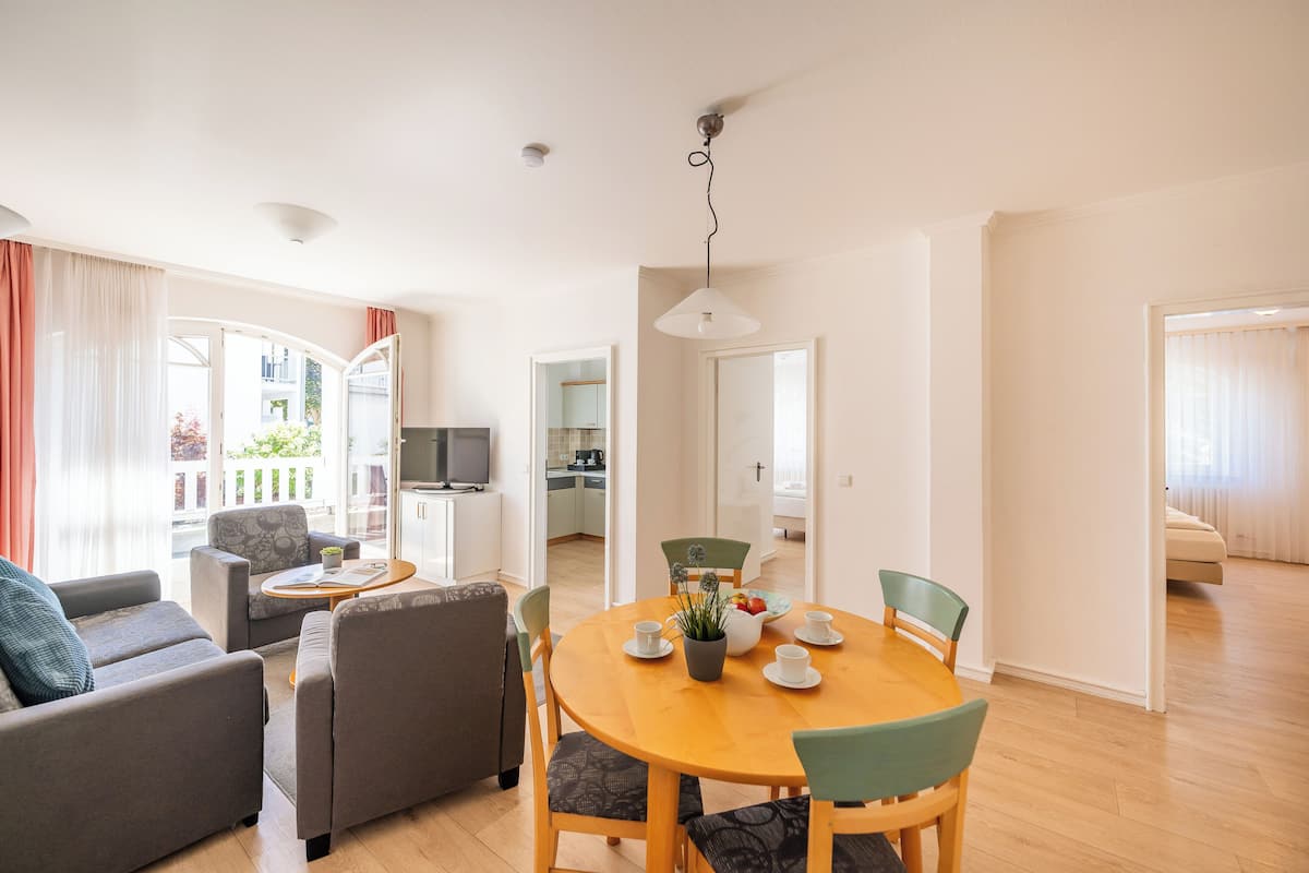 A modern living room with a round wooden dining table, grey sofas, and a kitchen in the background.