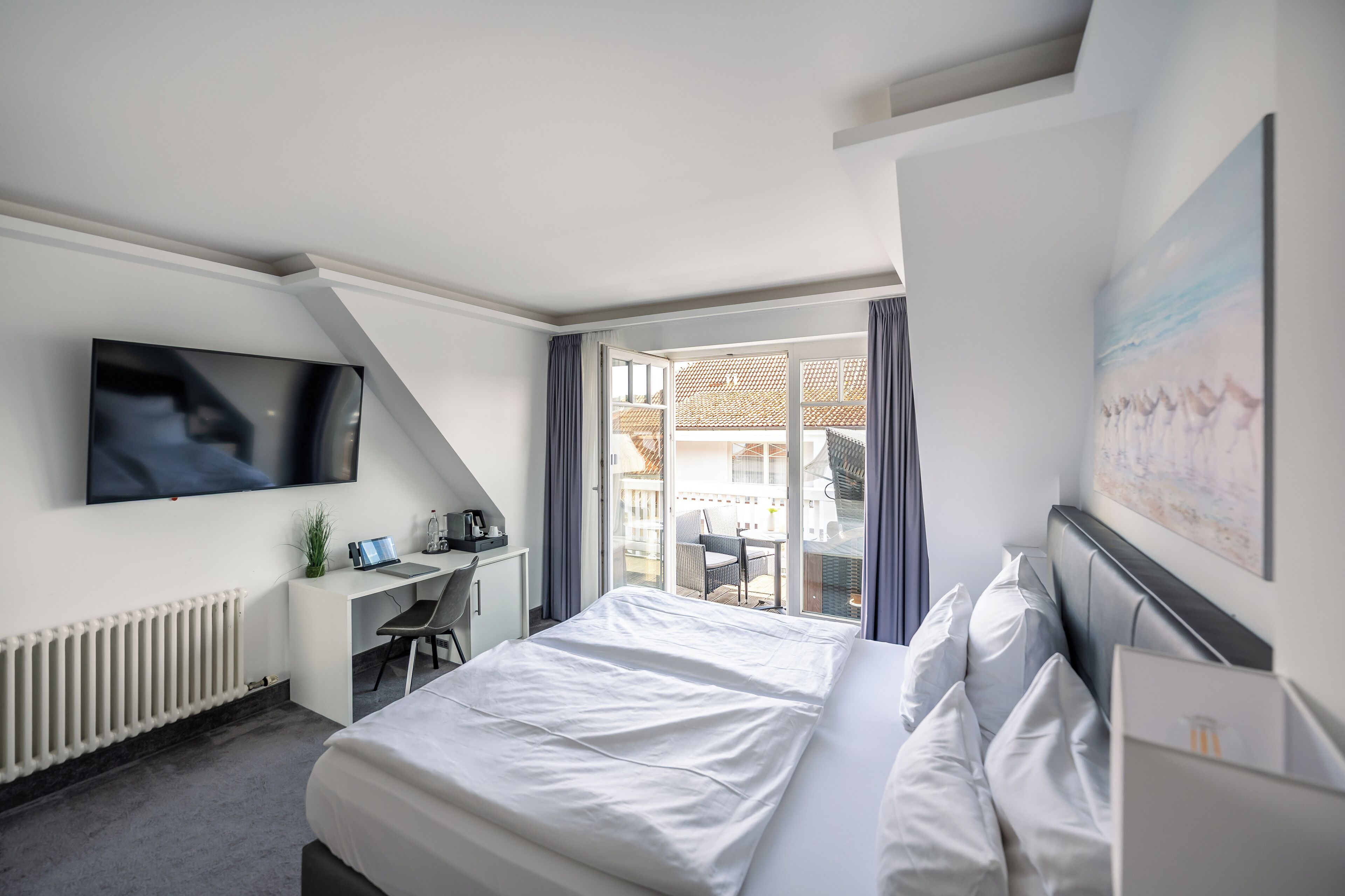Une chambre d’hôtel moderne dotée d’un grand lit, d’un bureau, d’une télévision et d’un balcon offrant une vue sur les bâtiments.