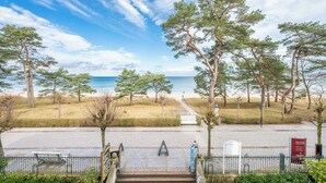Un sentier pavé mène à une plage d’où l’on a une vue sur la mer, et qui est entouré d’arbres et d’une clôture.