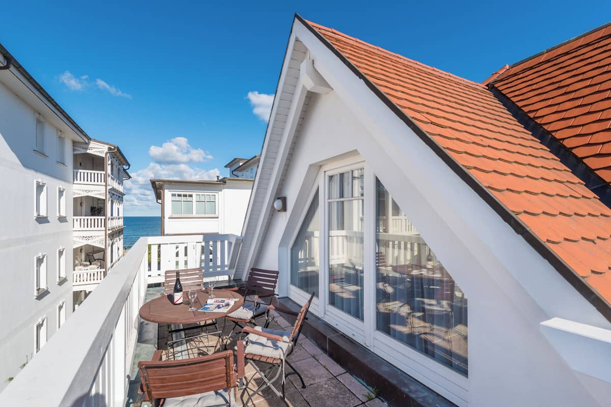 A balcony with a table and chairs, overlooking a residential area and the sea.