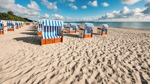Une plage bordée de rangées de chaises de plage et de parasols à rayures, une plage de sable fin et un ciel dégagé.
