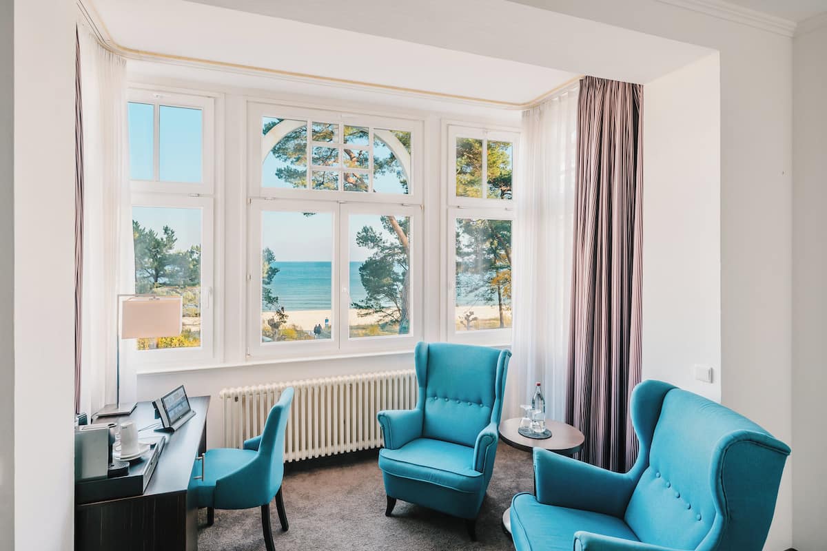 A room with a view of the sea, featuring a desk, two chairs, and a small table with a lamp.
