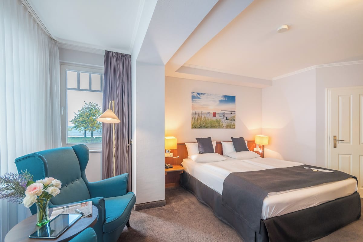 A hotel room with a bed, a desk with a lamp, a chair, and a window with curtains.