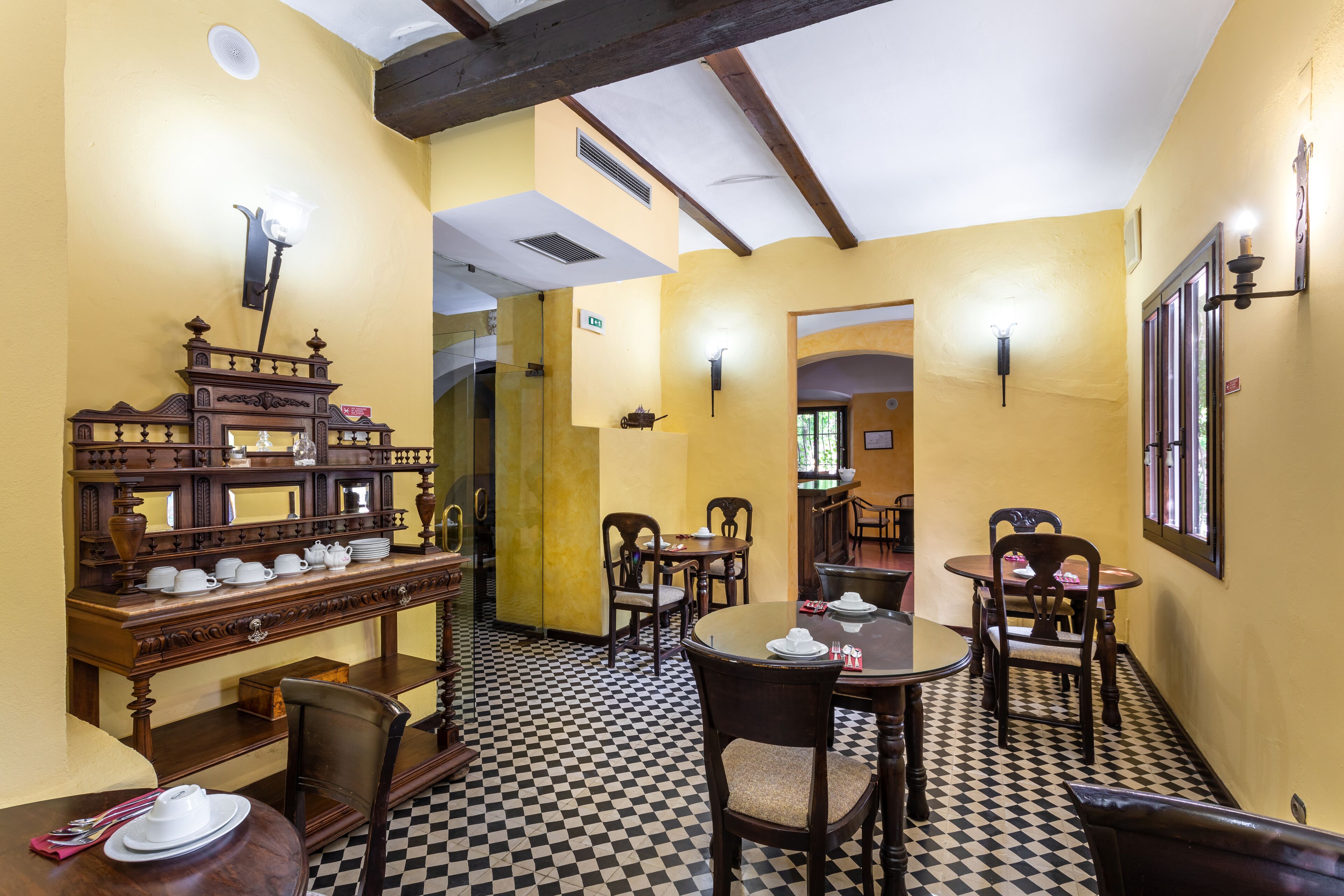 Un comedor con piso a cuadros, mobiliario de madera y lámparas fijadas a la pared.
