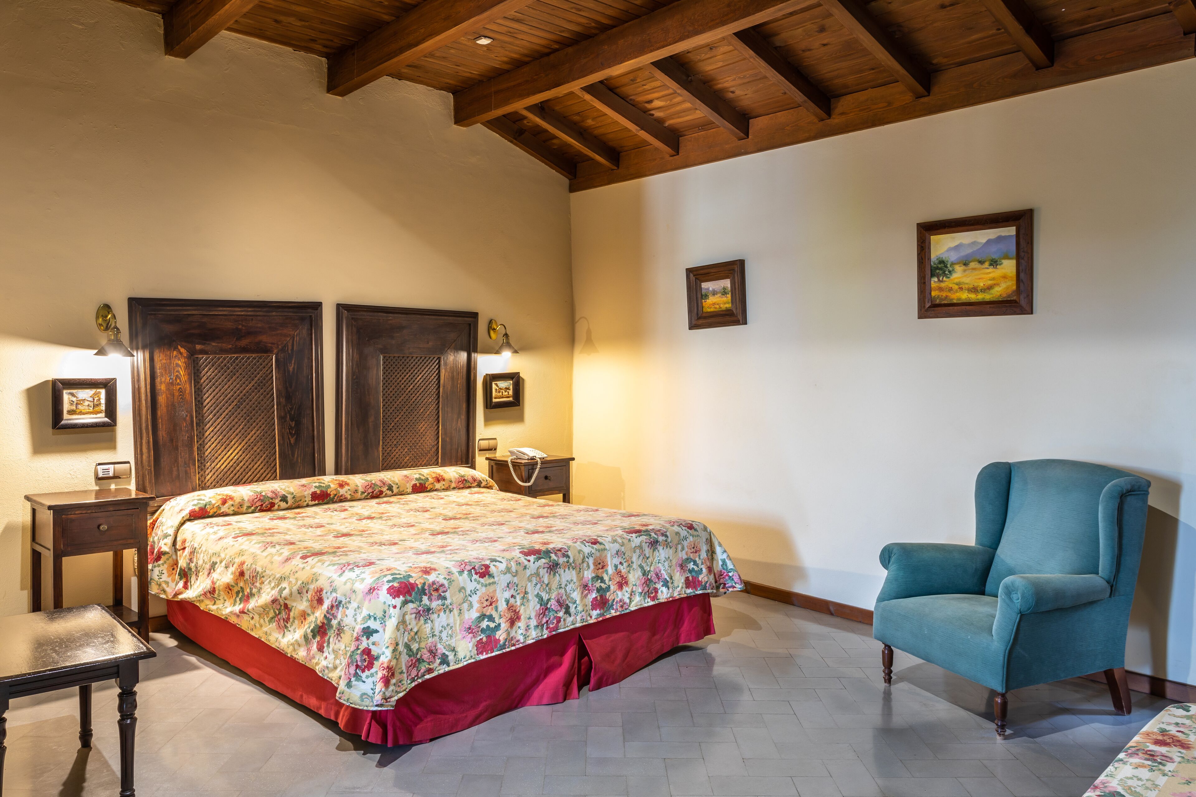 Un dormitorio con una cama grande, una silla, una mesita de noche y dos lámparas de pared.
