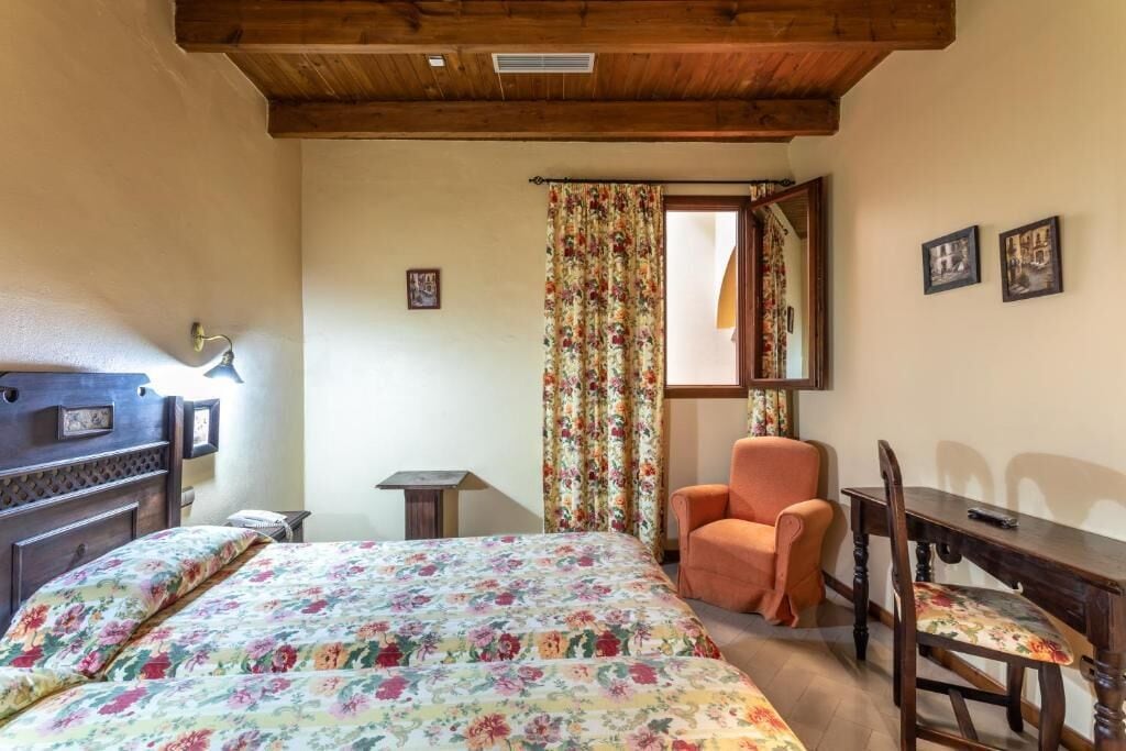 A bedroom with a bed, a chair, a small table, and a desk.
