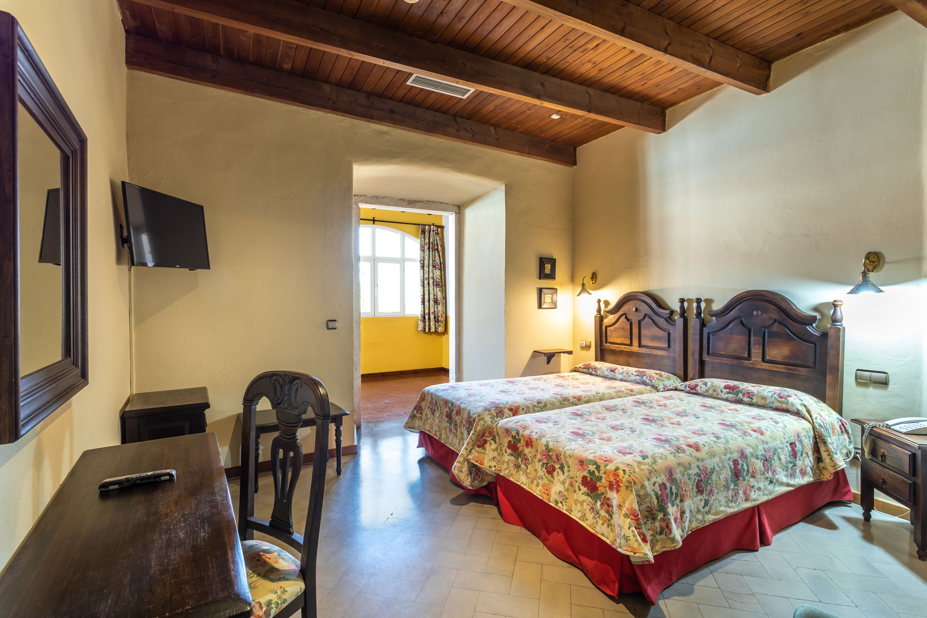 Un dormitorio con dos camas, cabeceros de madera, un escritorio, una silla y un televisor en la pared.