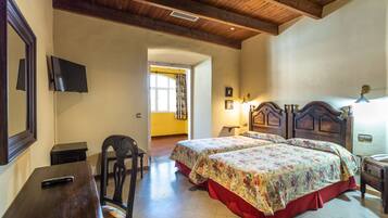 Un dormitorio con dos camas, cabeceros de madera, un escritorio, una silla y un televisor en la pared.