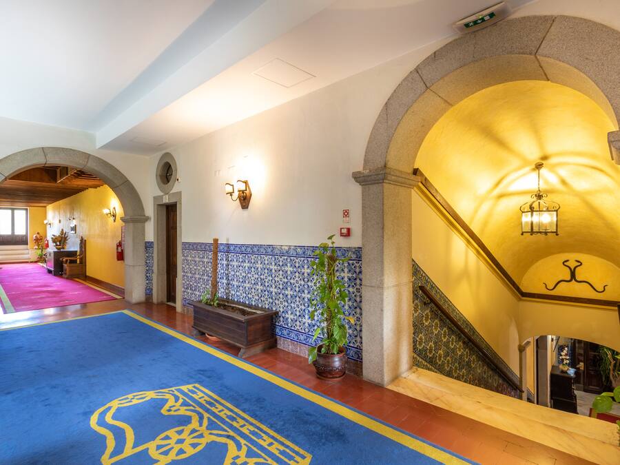 A hotel lobby with a blue carpet, a staircase with a yellow railing, and a wall with blue and white tiles.