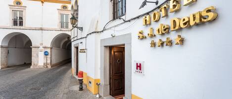 A hotel entrance with a sign reading "HOTEL S.J. de Deus" and a blue directional sign.
