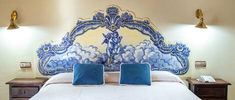 Een hotelkamer met een groot bed, twee nachtkastjes, een decoratief blauw-wit hoofdbord en wandlampen.