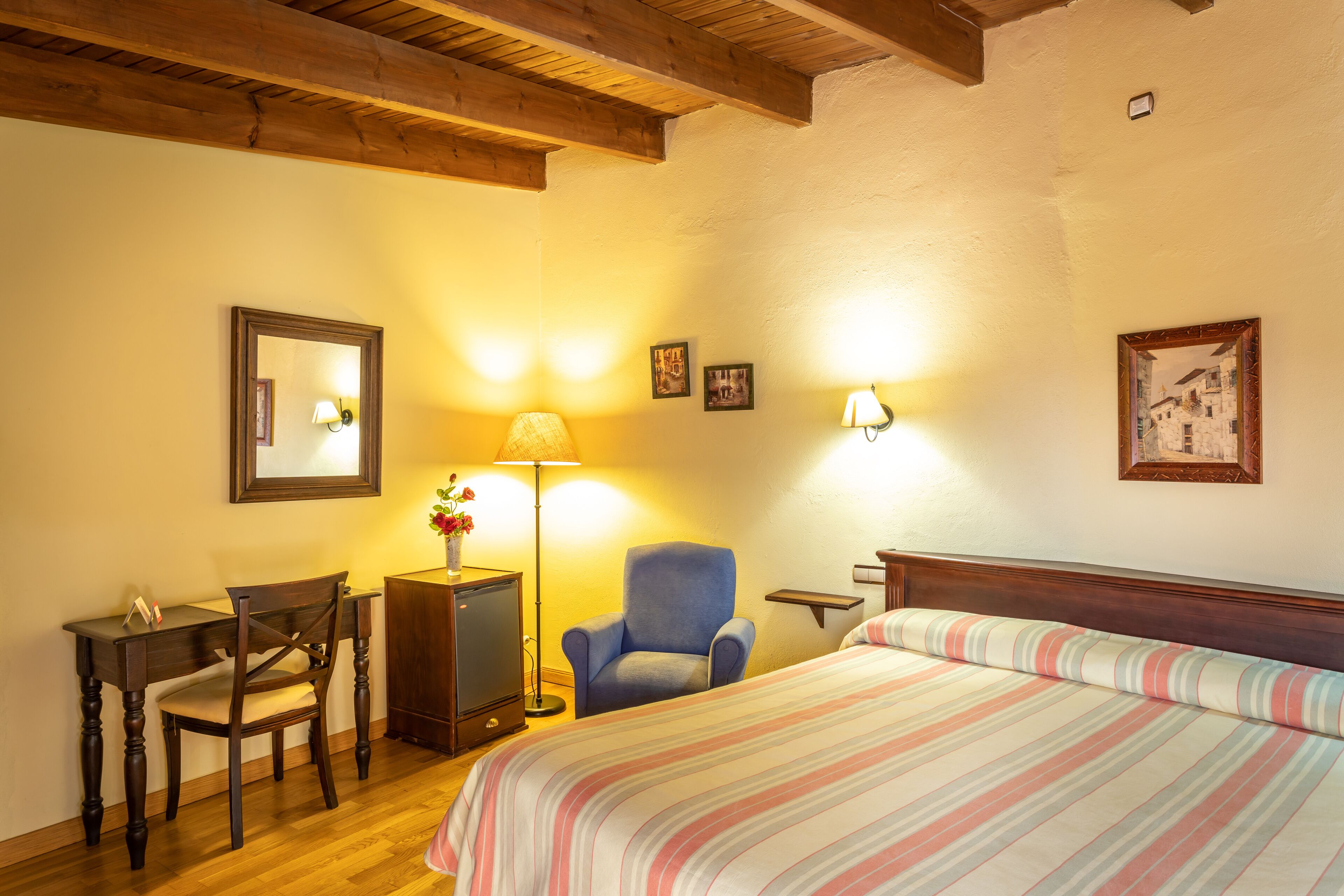 A bedroom with a bed, a desk, a chair, a lamp, and two wall-mounted lamps.
