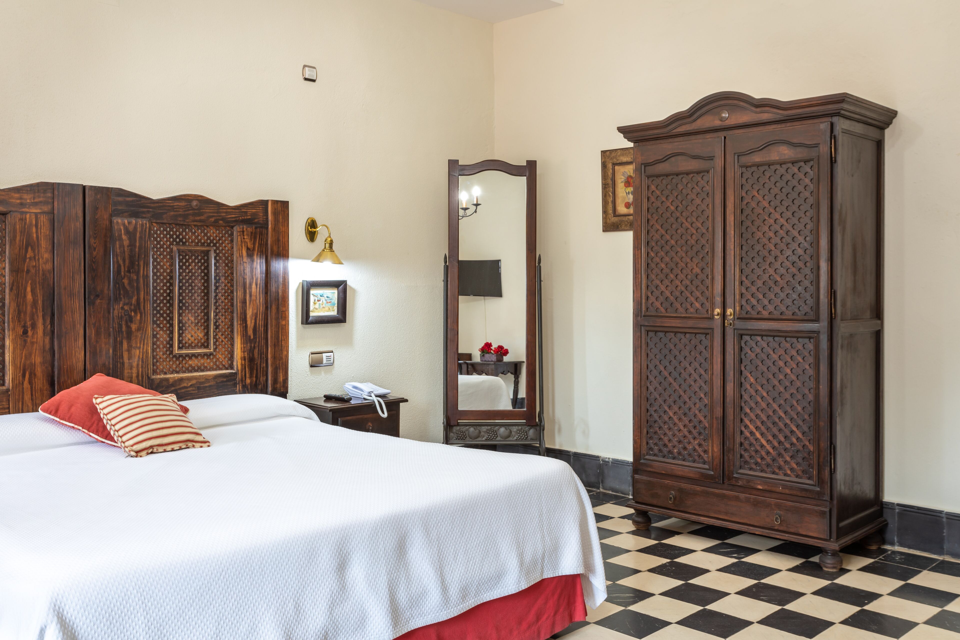 A hotel room with a bed, a wardrobe, a mirror, and a checkered floor.