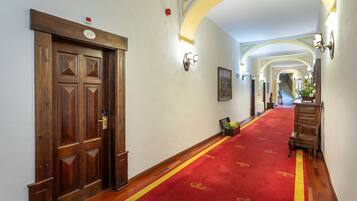 A hallway with a red carpet, wooden doors, and a staircase in the background.