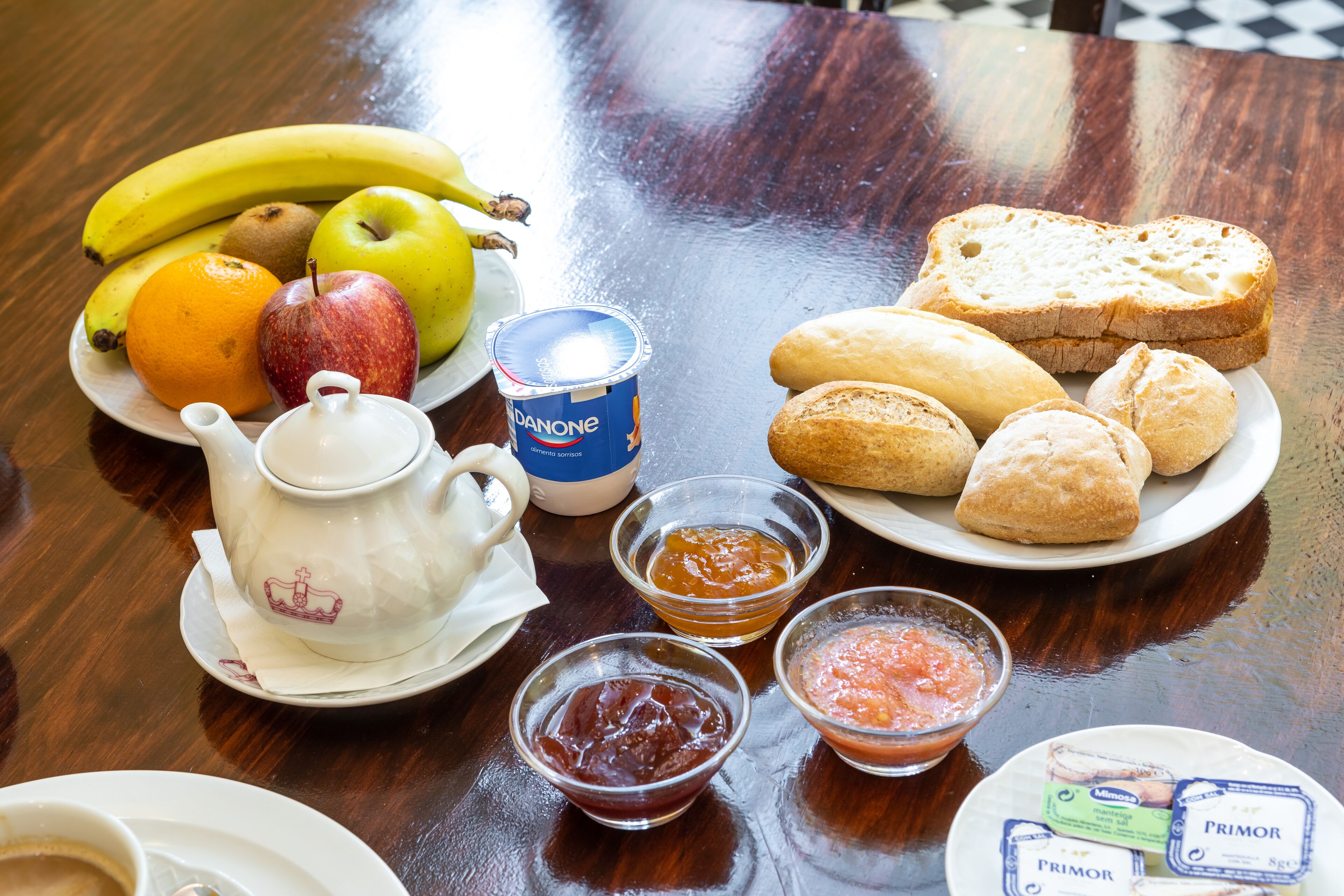 A table with a teapot, a plate of fruits, bread, and condiments.