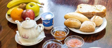 Une table avec une théière, une assiette de fruits, du pain et des condiments.