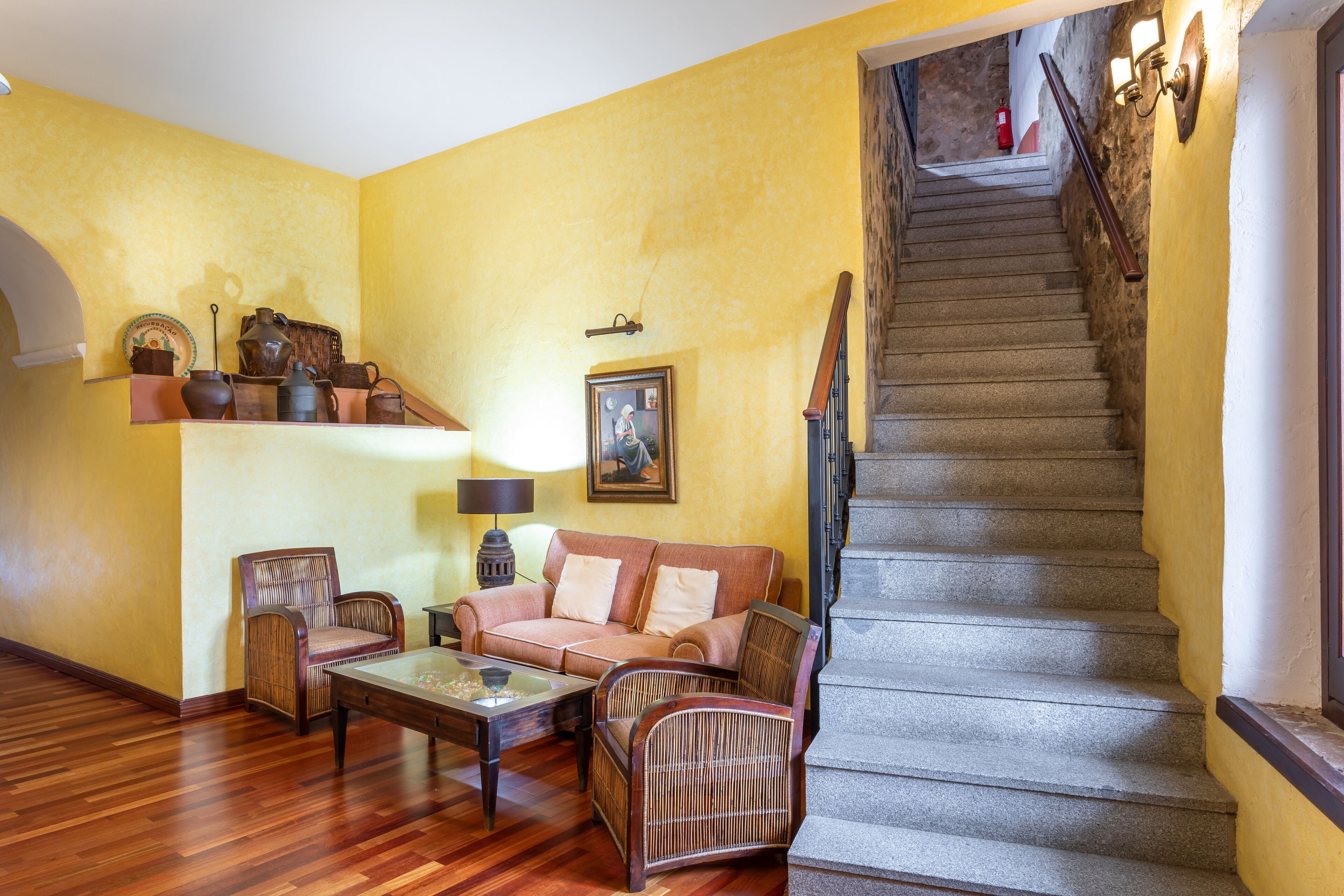 Una sala de estar con piso de madera, un sofá, dos sillas, una mesa de centro y una escalera con barandilla.