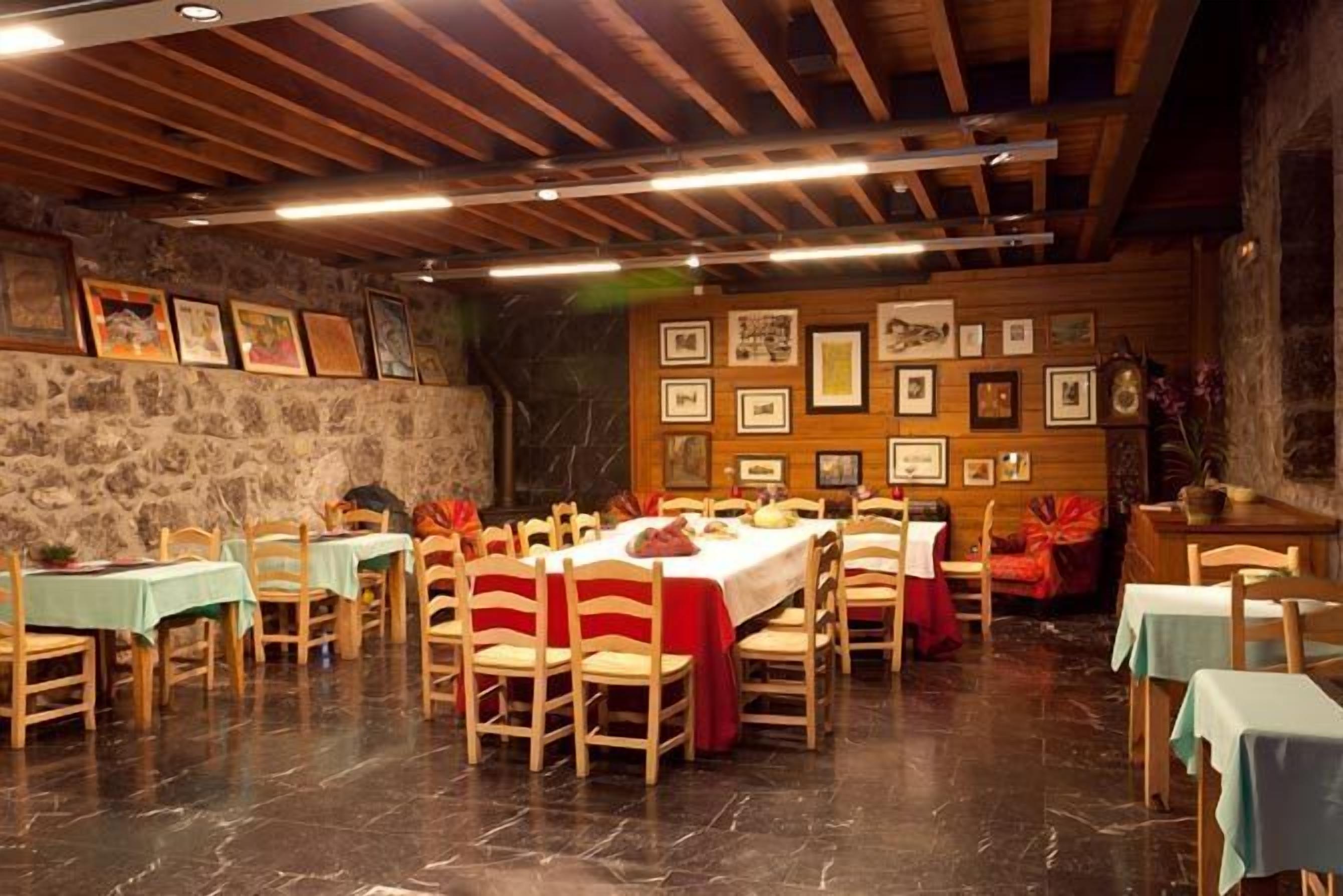 Un comedor con mesas y sillas de madera, paredes de piedra y cuadros enmarcados.