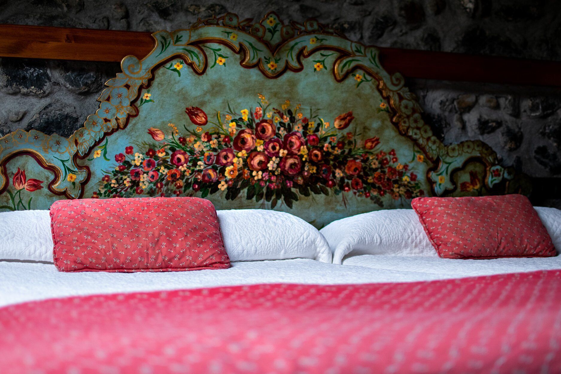 A bed with a floral headboard and red pillows.