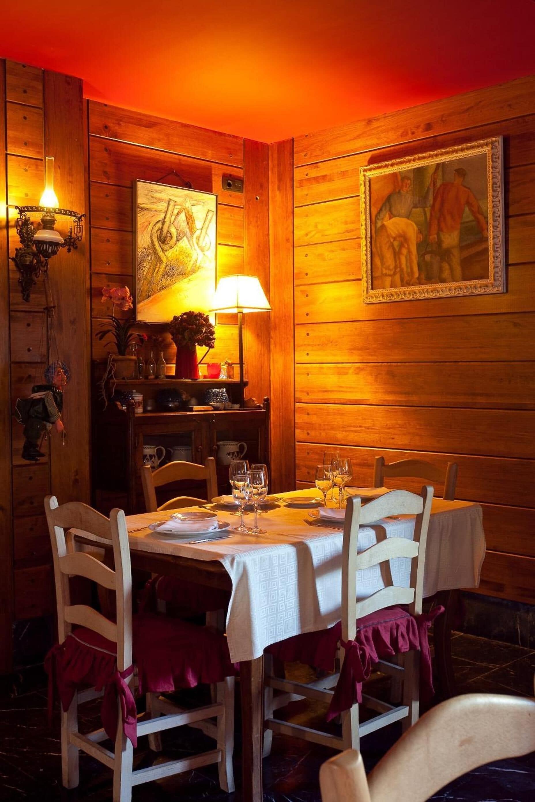 A wooden-paneled room with a dining table set for two, a lamp, and a framed painting on the wall.