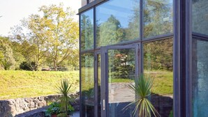 A modern building with large glass windows and stone walls, featuring potted plants on the ground.