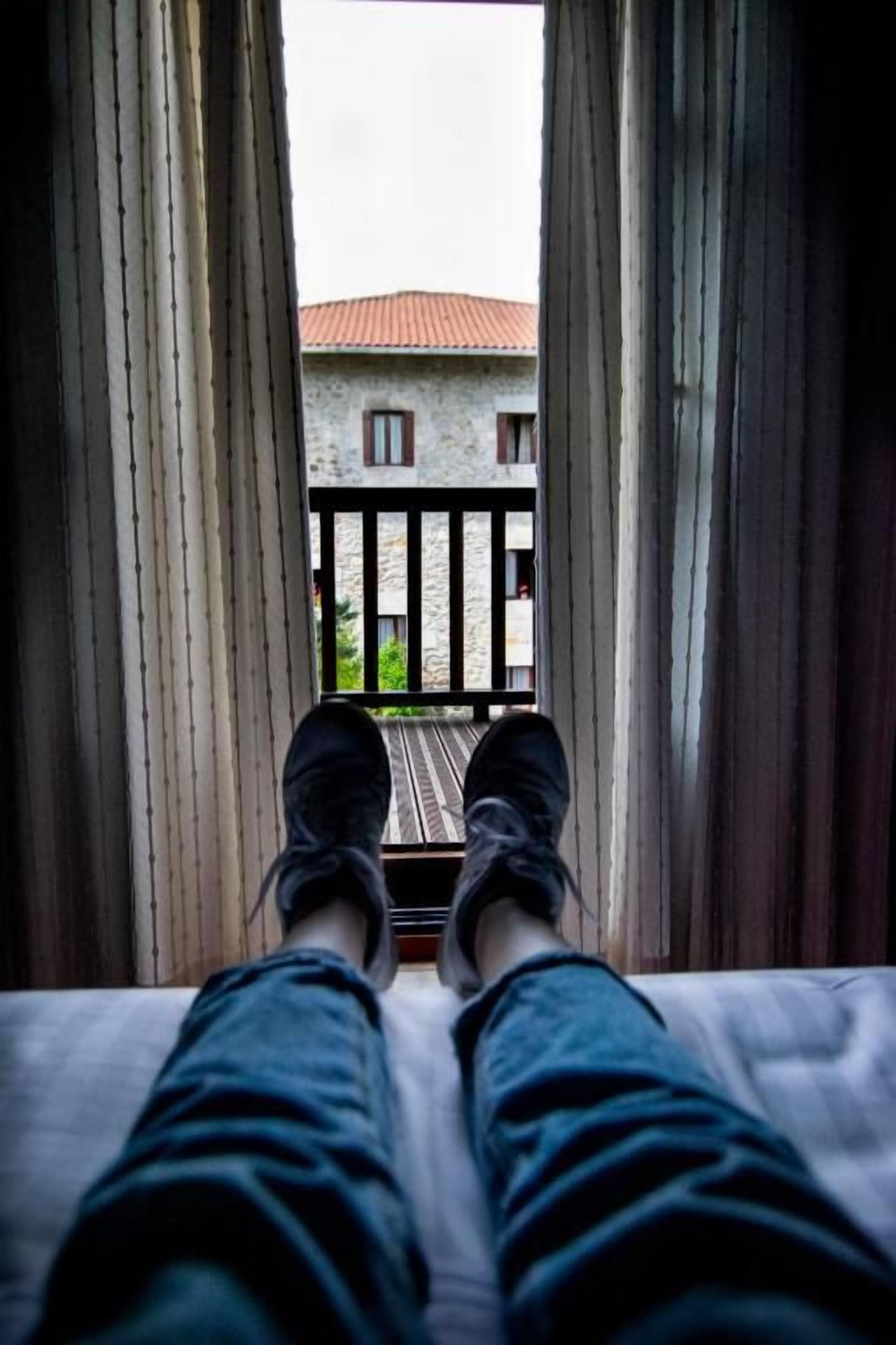 A bed with a view of a balcony and a building through curtains.