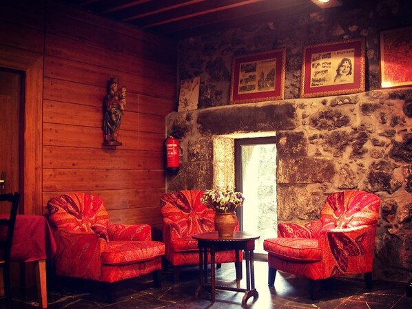 A cozy room with wooden walls, a stone fireplace, and red upholstered chairs. - Hotel Antsotegi (Etxebarria)