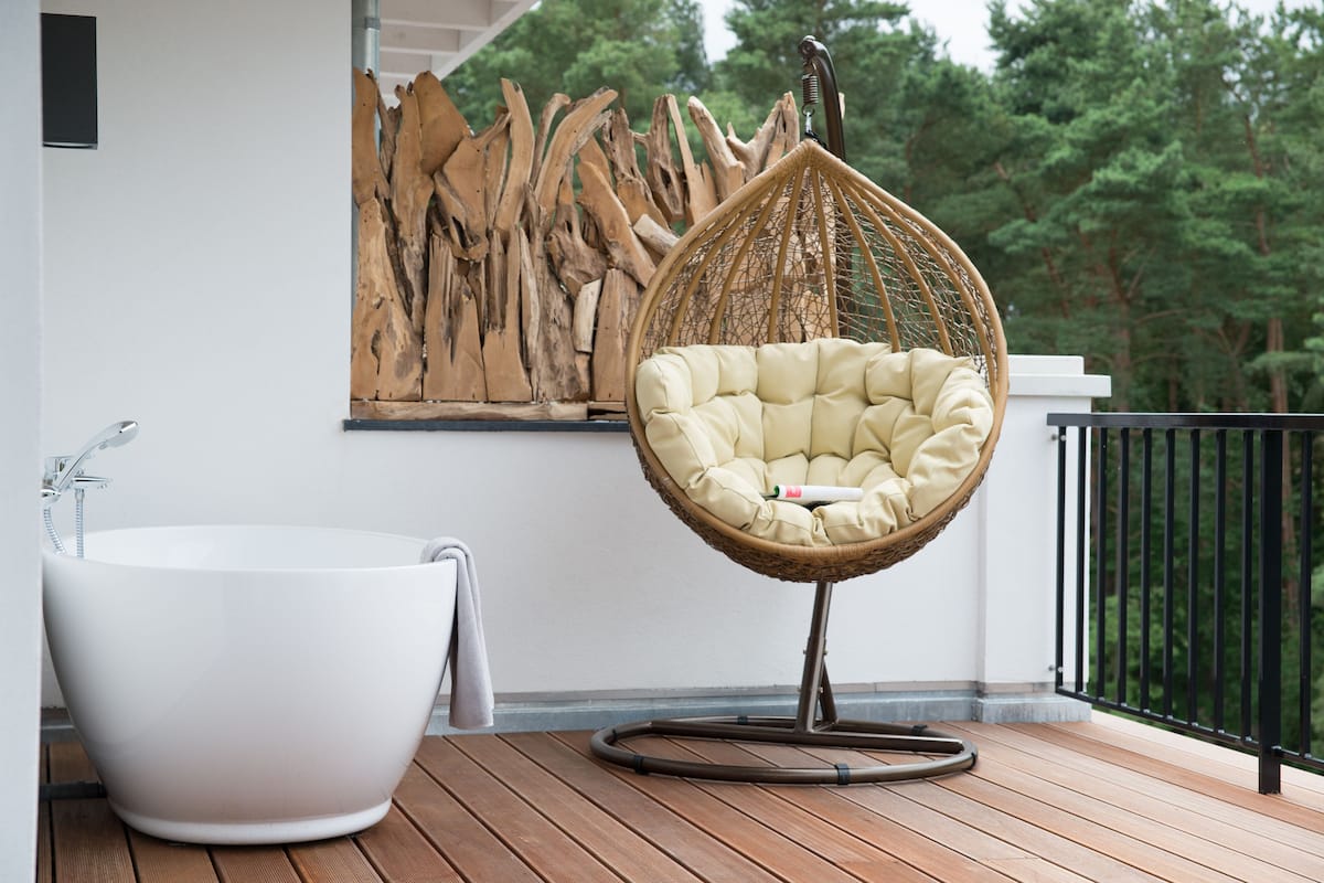 Une salle de bain moderne avec une baignoire sur pieds, un fauteuil suspendu en osier et une terrasse en bois.