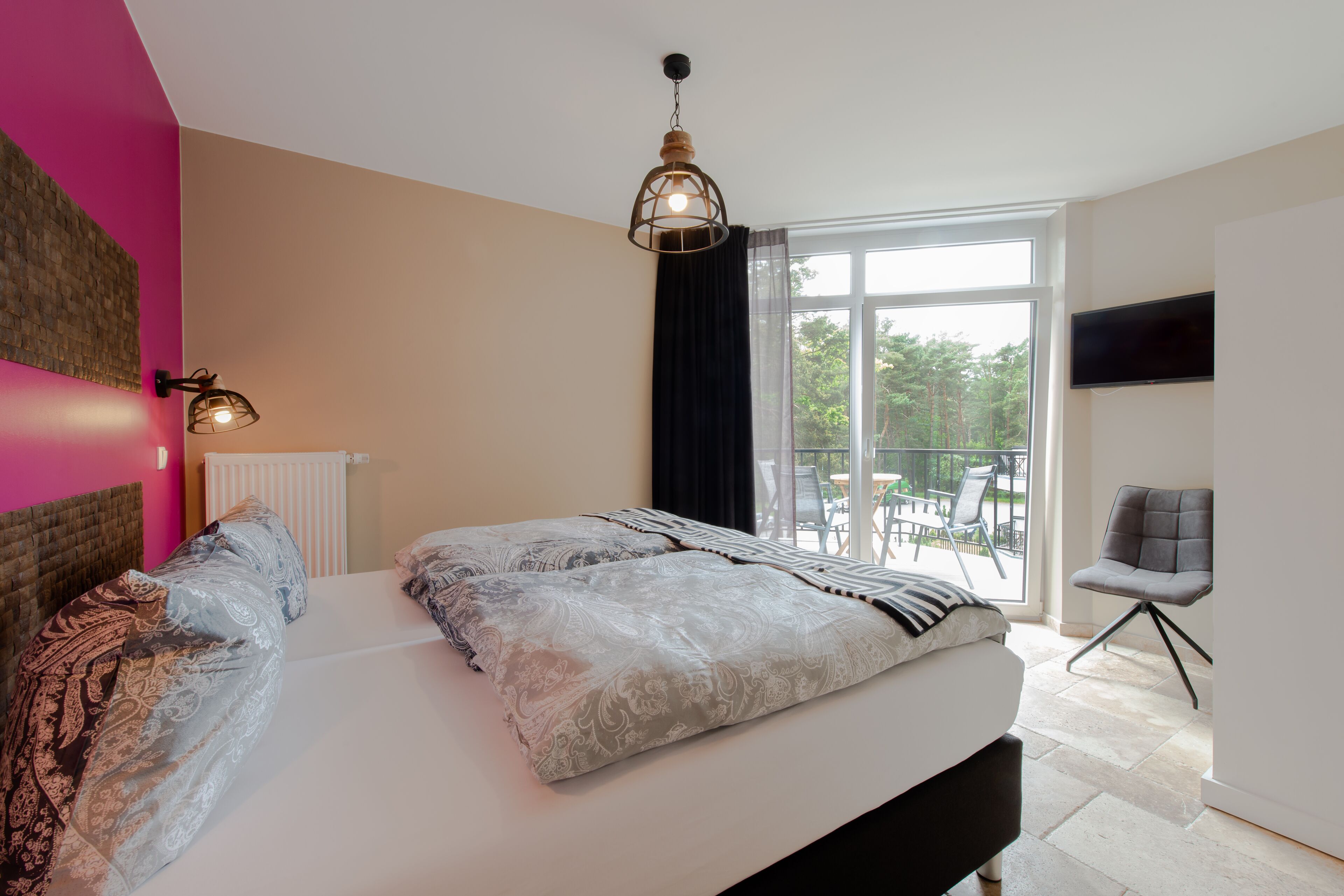 A bedroom with a large bed, a ceiling light, a TV, and a view of the outdoors.