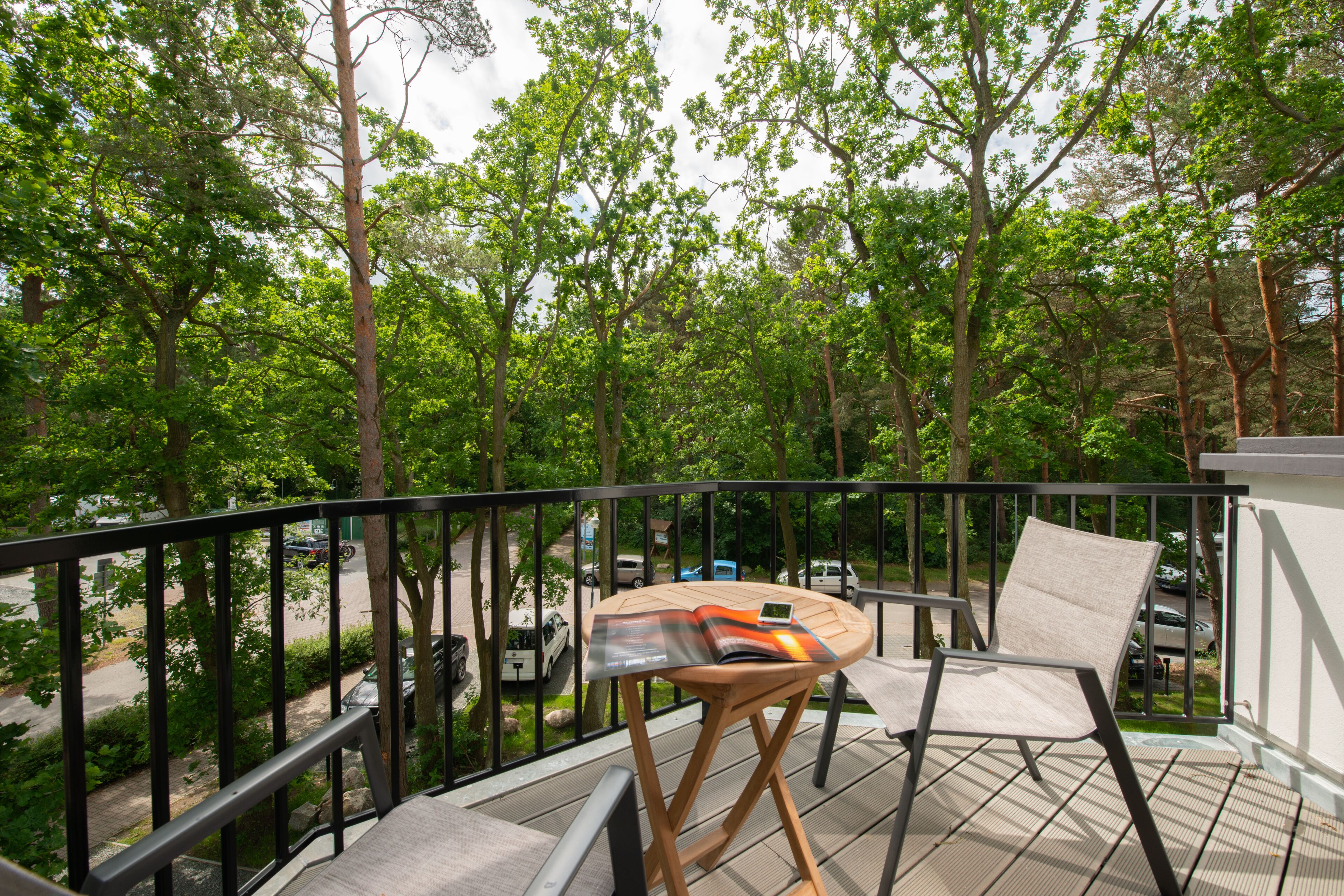 Een balkon met een tafel en stoelen, met uitzicht op een straat en bomen.