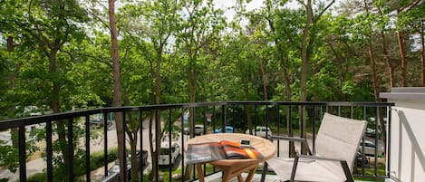 Een balkon met een tafel en stoelen, met uitzicht op een straat en bomen.