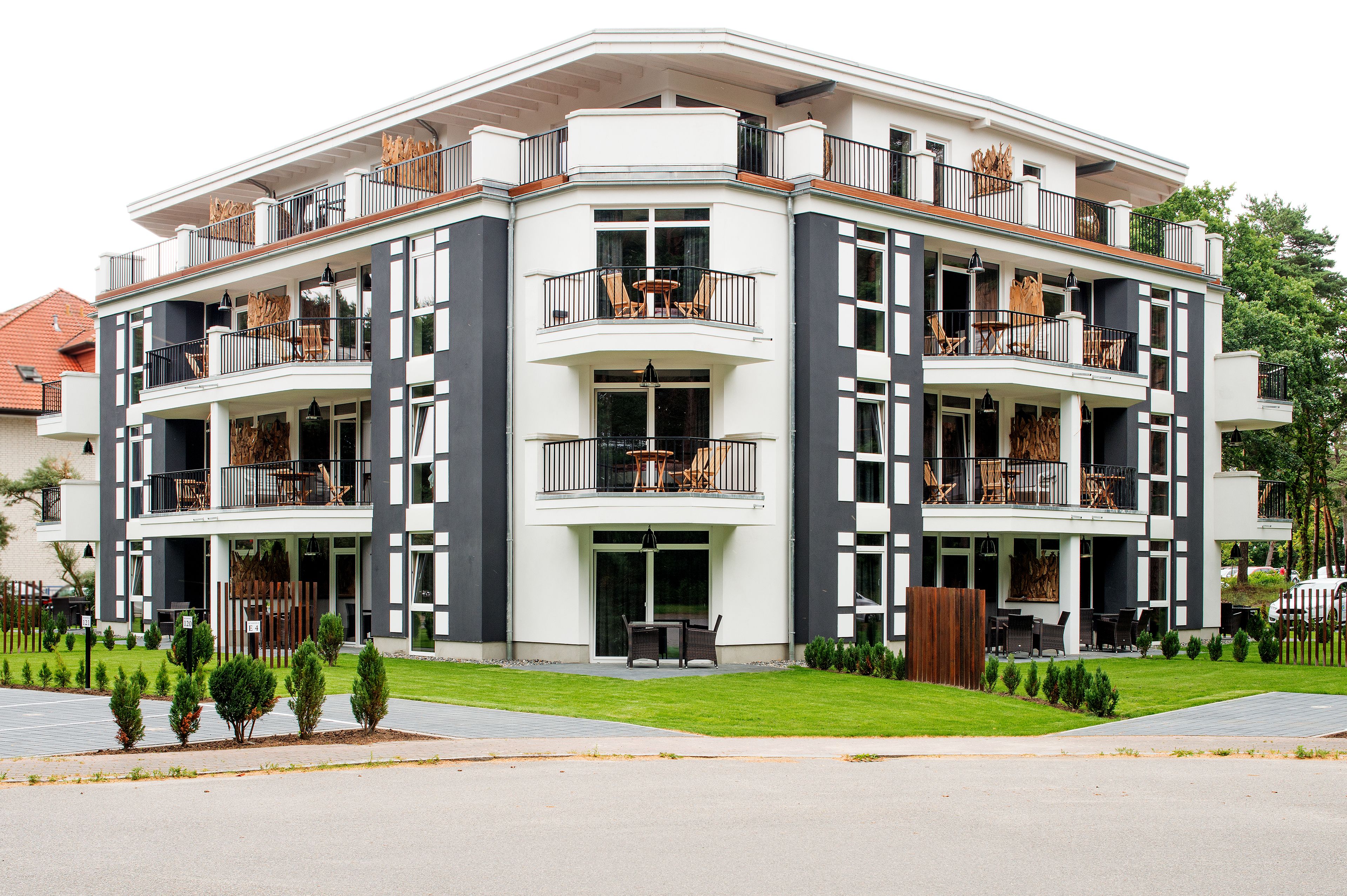 A modern multi-story building with balconies, outdoor seating, and a well-maintained lawn.
