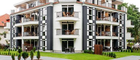 A modern multi-story building with balconies, outdoor seating, and a well-maintained lawn.