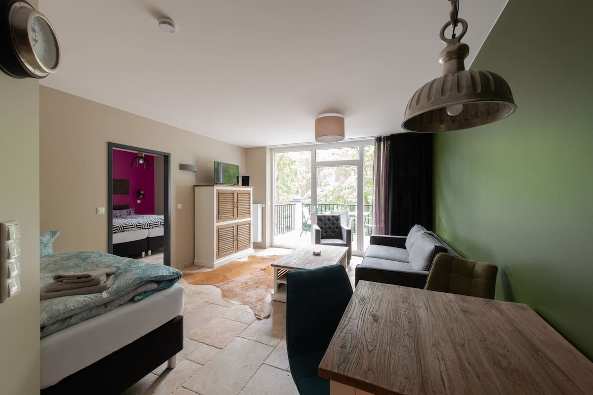 Une chambre moderne équipée d’un lit, d’une table à manger et d’un canapé. Une fenêtre laisse entrer la lumière naturelle et offre une vue sur l’extérieur.